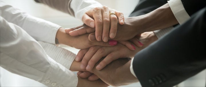 alt image text of hands inside of a team huddle to represent winning