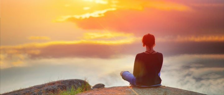 image of woman sitting on edge of cliff enjoying a sunset