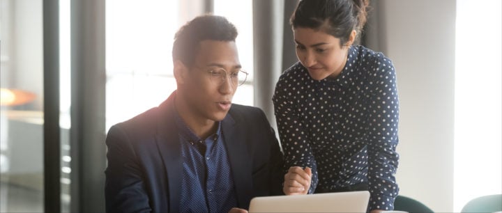 business woman coaching a business man and both looking at a computer