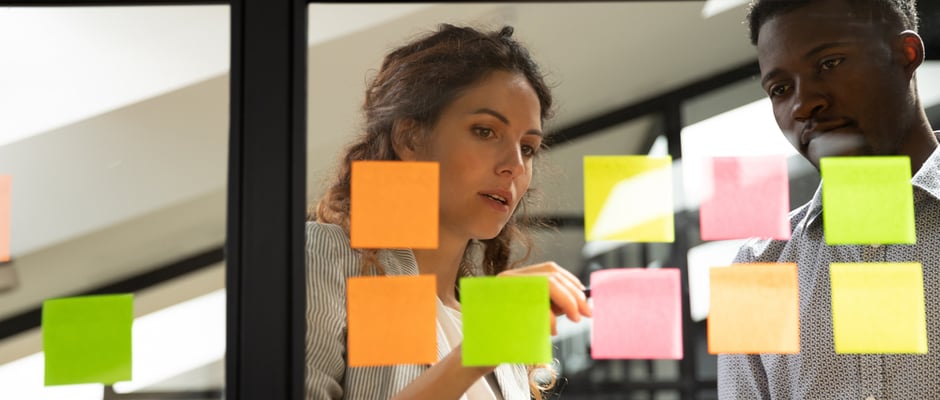 image of woman and man looking at sticky notes on a board to represent trying something different