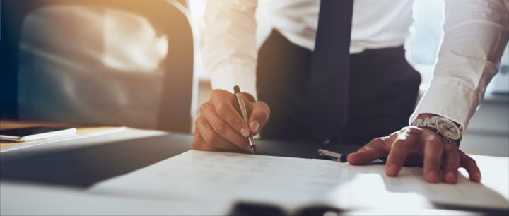 businessman standing at a desk signing papers
