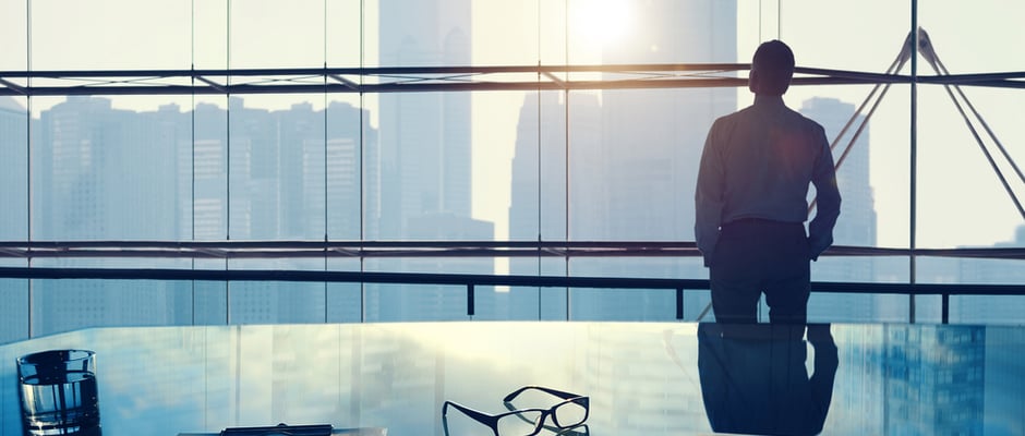 image of white collar businessman looking out a high rise office building window