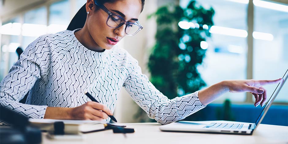 woman taking notes while using a laptop