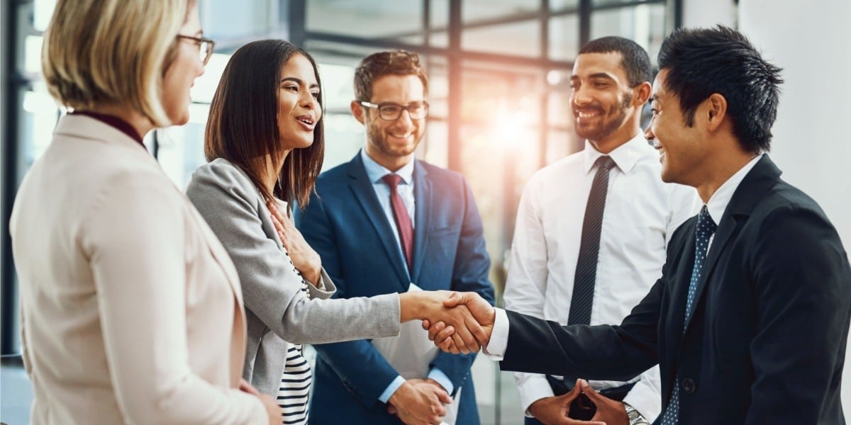 Businesspeople shaking hands surrounded by their peers