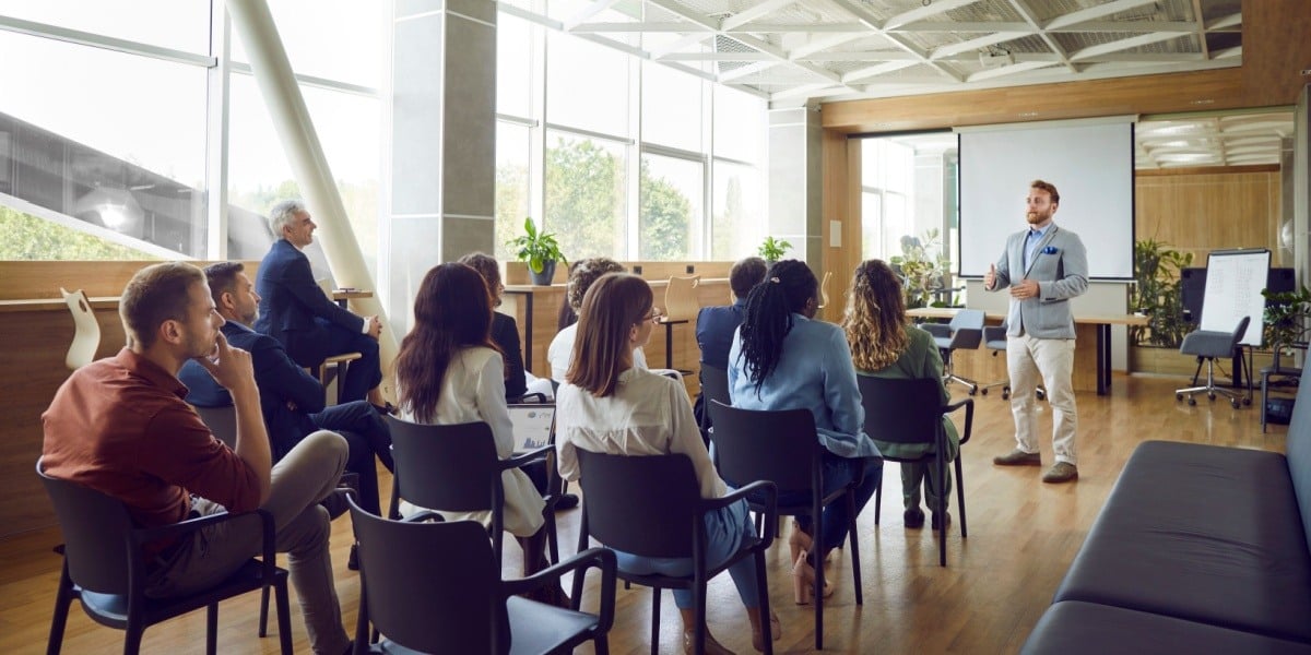 Businessman giving a sales training to a room of professionals sitting down