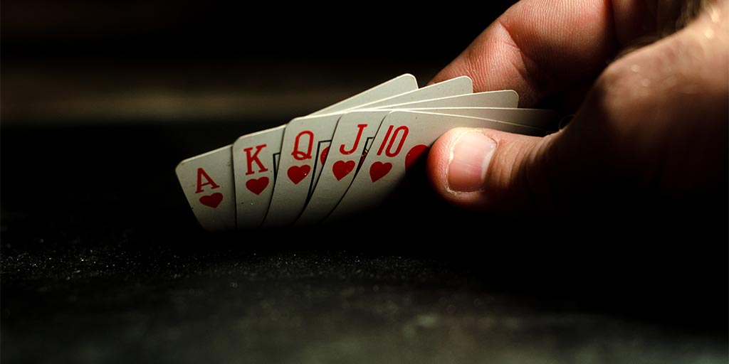 man holding playing cards with a royal flush poker hand 