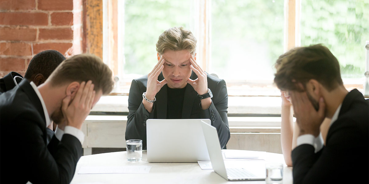 frustrated business people rubbing their heads sit around a table